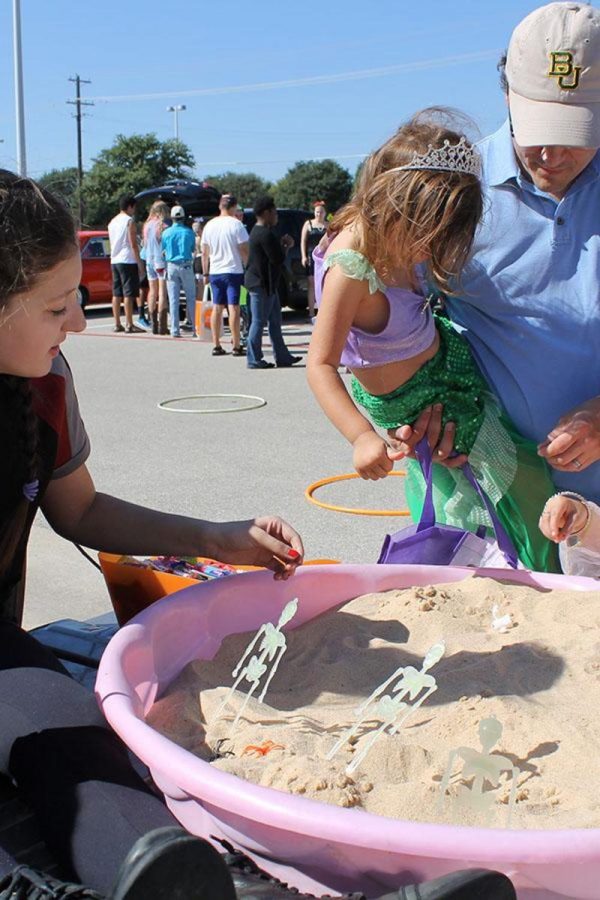 Sophomore Lindsey Foster helps young kids work with the sand pit.
Spanish Club is one of the clubs that participated in Trunk or Treat and they had a sand pit that kids could dig through and find little treasures. 
The children and their costumes are my favorite part because they are adorable, Ayah Alomari said. It truly makes your day.