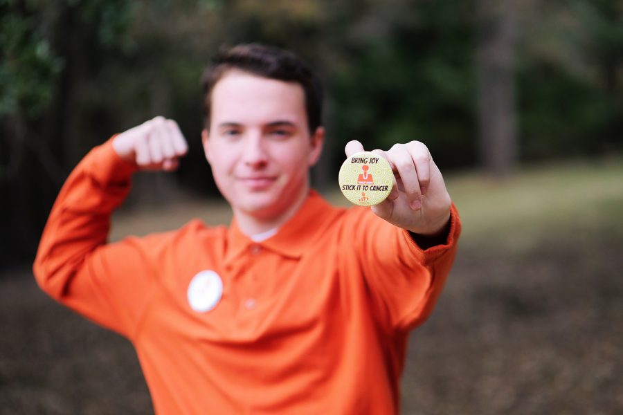 Senior Lance White holds up a Stick it to Cancer button that he made with his nonprofit, Lift Brigade.