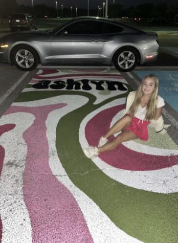 Ashlyn Gazlay poses with her brand new parking spot featuring her car in the background. Trying not to be basic, she said, she decided to mix her pink and green paint both with white to make two new colors and make the lines different sizes. “I looked up some ideas on Pinterest, but those were ones everyone was doing, so I decided to just use the two colors I wanted -green and pink- and just drew random, curved lines that were different sizes and added my name,” Gazlay said. “The process was pretty long and took four separate days to do it.”
