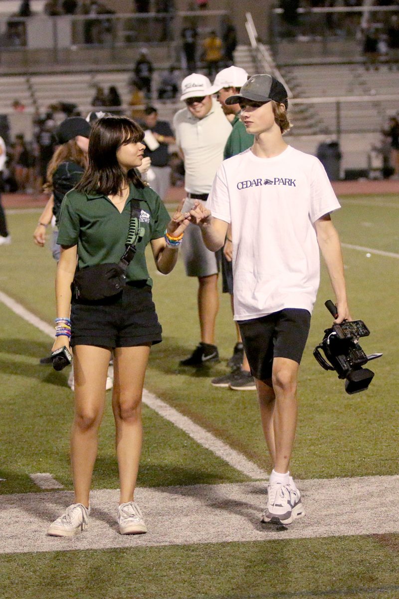 Cameras in hand, junior Reese Elizondo and sophomore Reid Cummins, members of The Wolfcast broadcast staff, walk off the field after the school fight song. Elizondo is in charge of keeping the stories on the CPHSNews Instagram account updated throughout the games and helps create each week’s hype video.  
“I love the thrill of it,” Elizondo said. “I’ve loved sports for a long time, so being on the field has always been something that I’ve wanted to do. I find it really fun. Depending on how the game’s going, any play could be the play of the game.” Photo by Willa Pursley