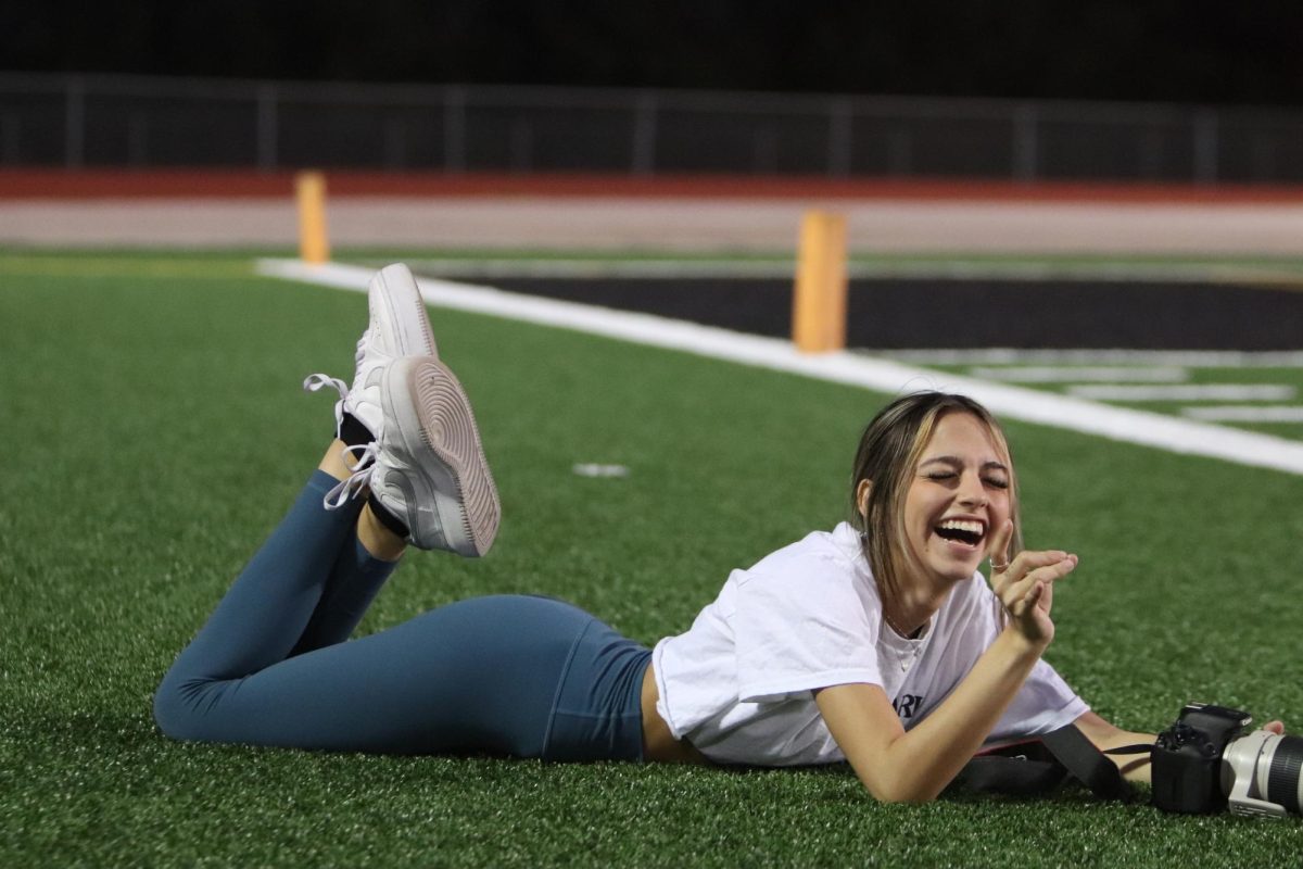 Laughing while laying on the football field for a better camera angle, senior Tylie Biggs, Tracks Yearbook Design Editor, takes pictures at the JV football game against Hendrickson on Oct. 12. The journalism programs work year round to provide continuous coverage over the events happening in the community. “I think it is important to have journalism kids and others in broadcast out there [on the football field] because I know when we’re out there, even during the bad times of the game, it helps having us around the team and supporting them,” Biggs said. “They can’t hear everything happening in the stands, so having us there to keep the team going and encouraging them really does mean more to them than we think.” Photo by Jane Yermakov
