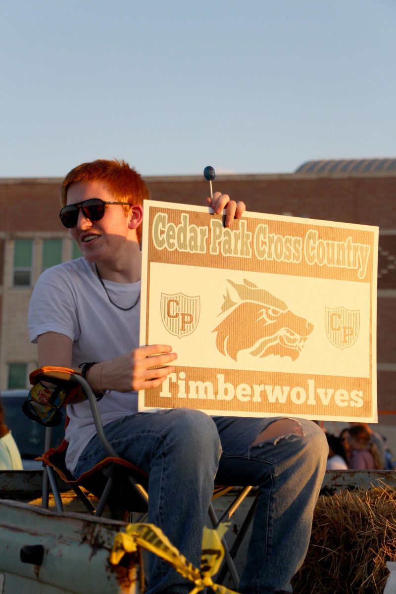 Sitting by his Trunk or Treat booth, sophomore Jackson Holmes promotes cross country to middle school students by holding up a sign. Holmes said he enjoyed sharing his hobby of running with the younger kids at this event. “Cross country is very therapeutic,” Holmes said. “My favorite part is [being with] the group of people. We all run together as a pack.”