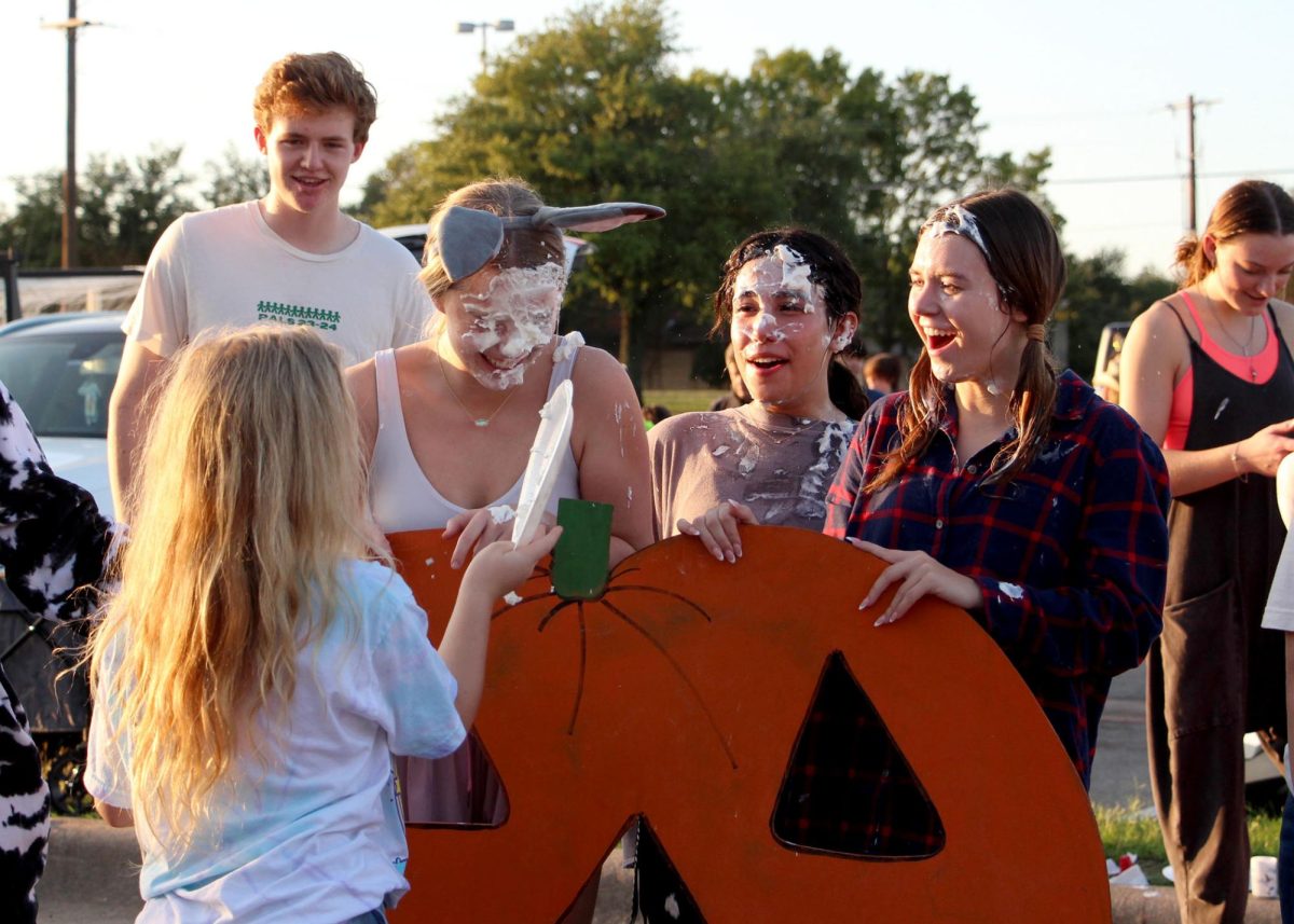 Squeezing her eyes shut and laughing, junior Sophia Orawetz, accompanied by several other seniors, gets pied in the face during the trunk or treat. The trunk or treat was a chance for all organizations to come together and enjoy their time with other students while promoting their organizations. “I had a lot of fun,” Orawetz said. “I was there representing PALs, and we had a little cakewalk station set up. I wanted to be pied and so did my friends, so we walked over to the pie station and I [let the kids] pie me.”