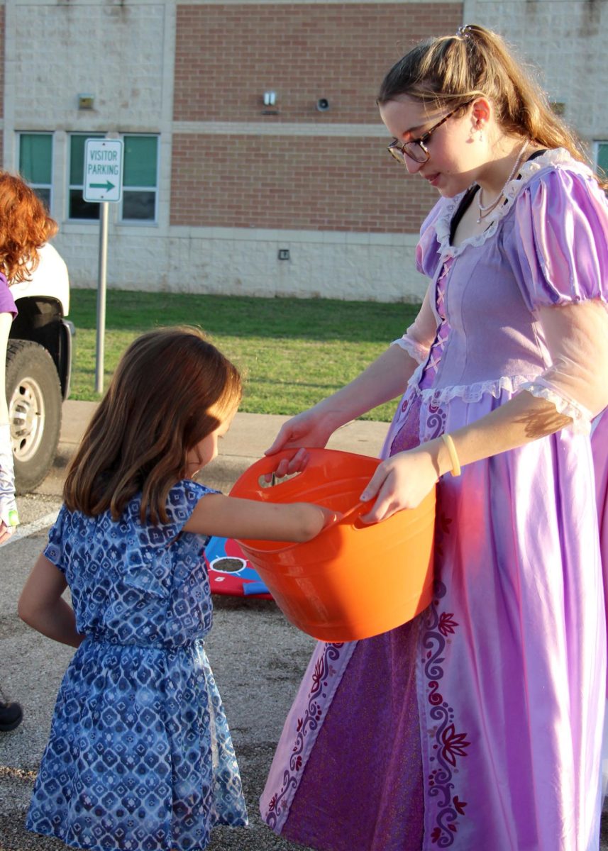 Presenting a bucket of candy to a young girl, Senior Courtney McDanald wears a princess dress as she runs the choir booth for Cedar Park’s annual trunk or treat on Oct. 26. McDanald is the choir president, and she explained that by wearing the princess dress she was advertised for princess tea, an annual choir event with the children. “The kids were so sweet,” McDanald said. “[As we played] the games with them, some of them were just so silly.”