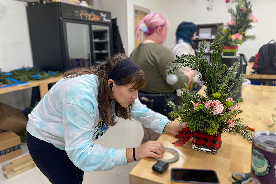 Wrapping the fabric around the vase, senior Lillian Dodds works on the December arrangement for the Flower Pack subscription. “I think its really important to get kids really interested in something because a lot of people take floral design just for like the art credit,” Dodds said. “But I think if theres a lot of money going into it and people can see how cool floral design is, then that can really inspire a lot of kids to maybe want to be florists.”