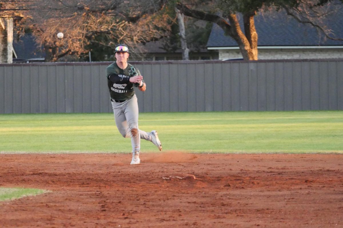 Throwing the ball, sophomore shortstop and third baseman Hudson Cuevas completes a play to first base at the scrimmage against Round Rock on Feb. 4. Installation of new turf on the fields has relocatedthe team to practicing on the grass fields and at a batting cage center off of Lakeline called D-Bat. “Our players have attacked this challenge,” Head Coach Ben Huffman said. “We’re just having to shift locations from a day to day basis. [But], the boys come out and wherever and whatever we’re doing they just try to get better every day.” 