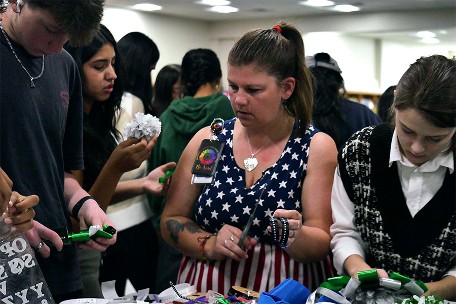 Students gather around a table selecting ribbons, trinkets, and supplies as they work on creating their own homecoming mums during the Den activity period. The Den hosted a mum-making event where students could share materials and ideas while learning how to make their own mums from scratch. “For mums, to buy all the stuff to make your own from scratch is really expensive,” Librarian Keri Burns said. “But if everybody has a couple of little things to offer and then everybody kind of makes it a group activity and shares, then the cost is divided and the fun is multiplied.”