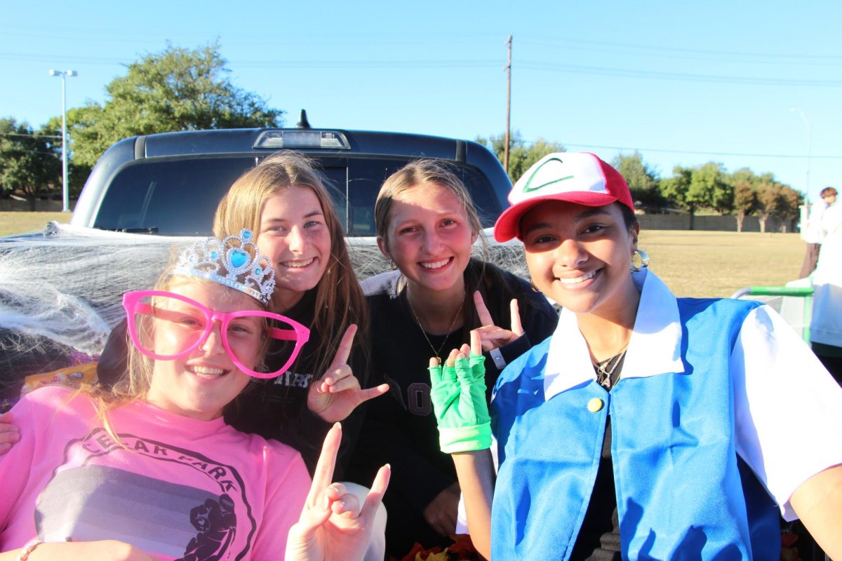 Smiling for the camera, girls' soccer players sophomore Ryan Haskins, juniors Anna Geertsema and Bella Ballenger, and senior Aerin Tryals-Meyer await visitors to their trunk. The team used a truck bed and filled it with candy, and covered the whole truck in spider webs to appeal more to the kids. “We have a scoring goal so you can shoot, or the kids can shoot,” Tryals-Meyer said. “Whenever they make it, they get candy.” 