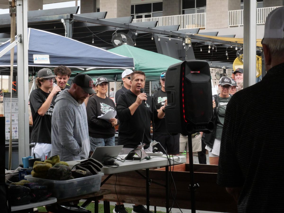 Holding a microphone, baseball booster club president Chris Cuevas announces the beginning of the annual cornhole tournament. The event has been held for the past two years and is designed to raise money for the baseball program in a fun way. “We’re a baseball team, so people love to compete,” Cuevas said. “So we figured we better do something that gets [their] attention. They want to compete. It’s not a hard sport to do, and we have all different [skill] levels [of participants].” Photo by Henry Mueller